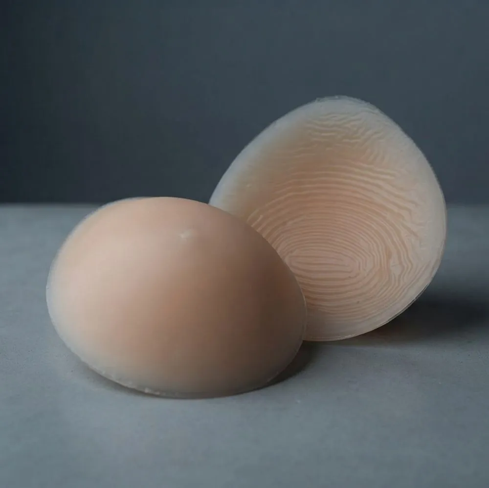 Two oval breast forms, one standing to show the textured back